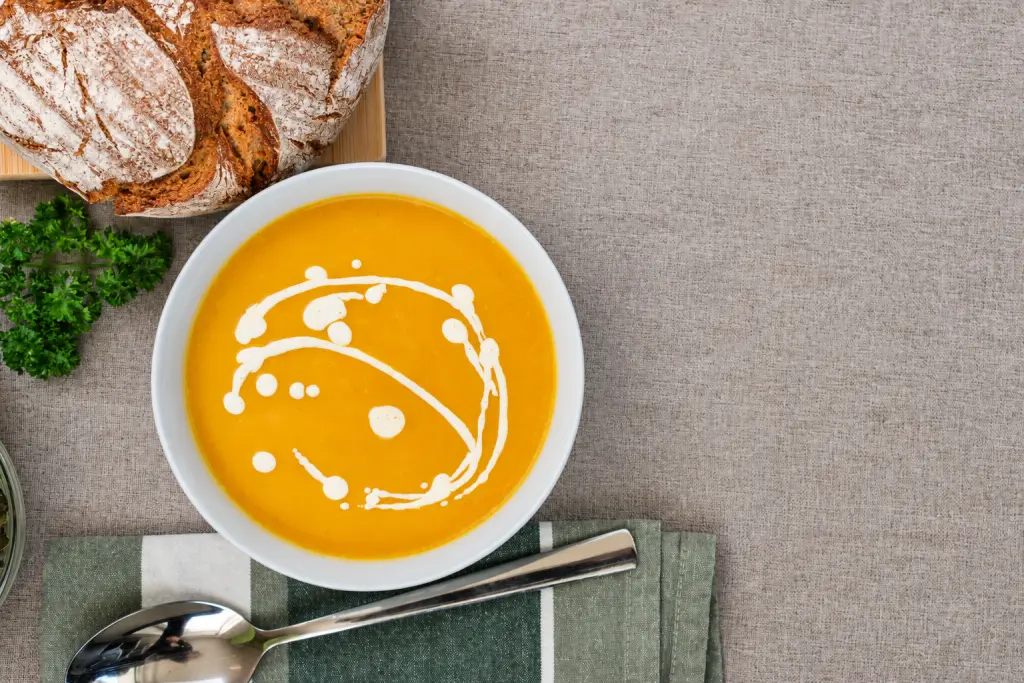 Creamy pumpkin soup served with rustic bread on a neutral linen table